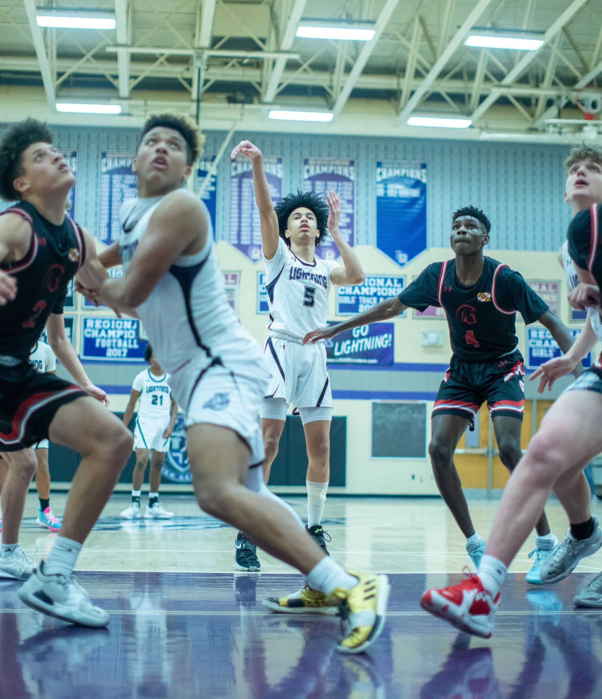 Basketball players jumping for a rebound in an indoor gym, with a referee in the background