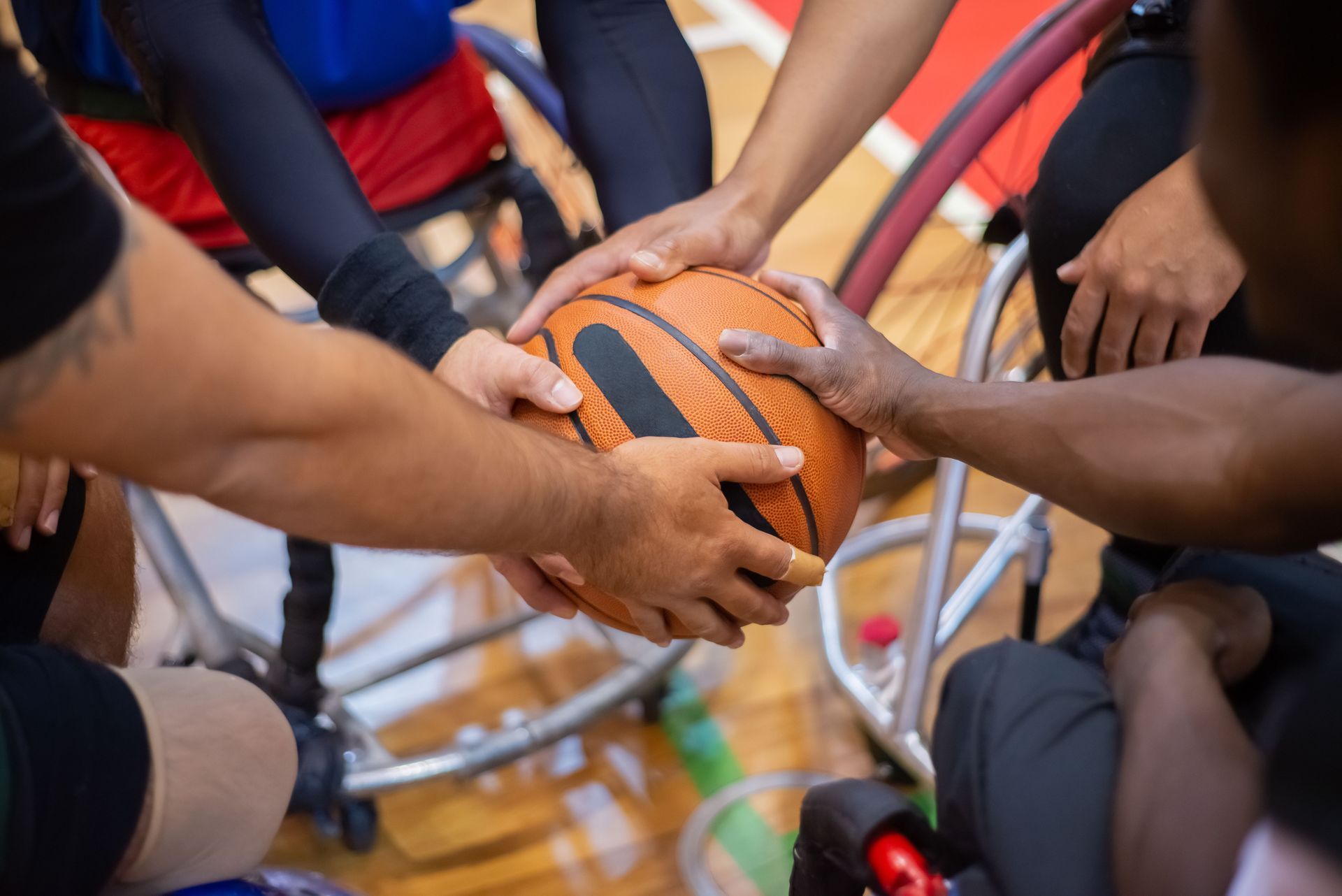 Hands reaching for an orange basketball in a wheelchair sports game on a court