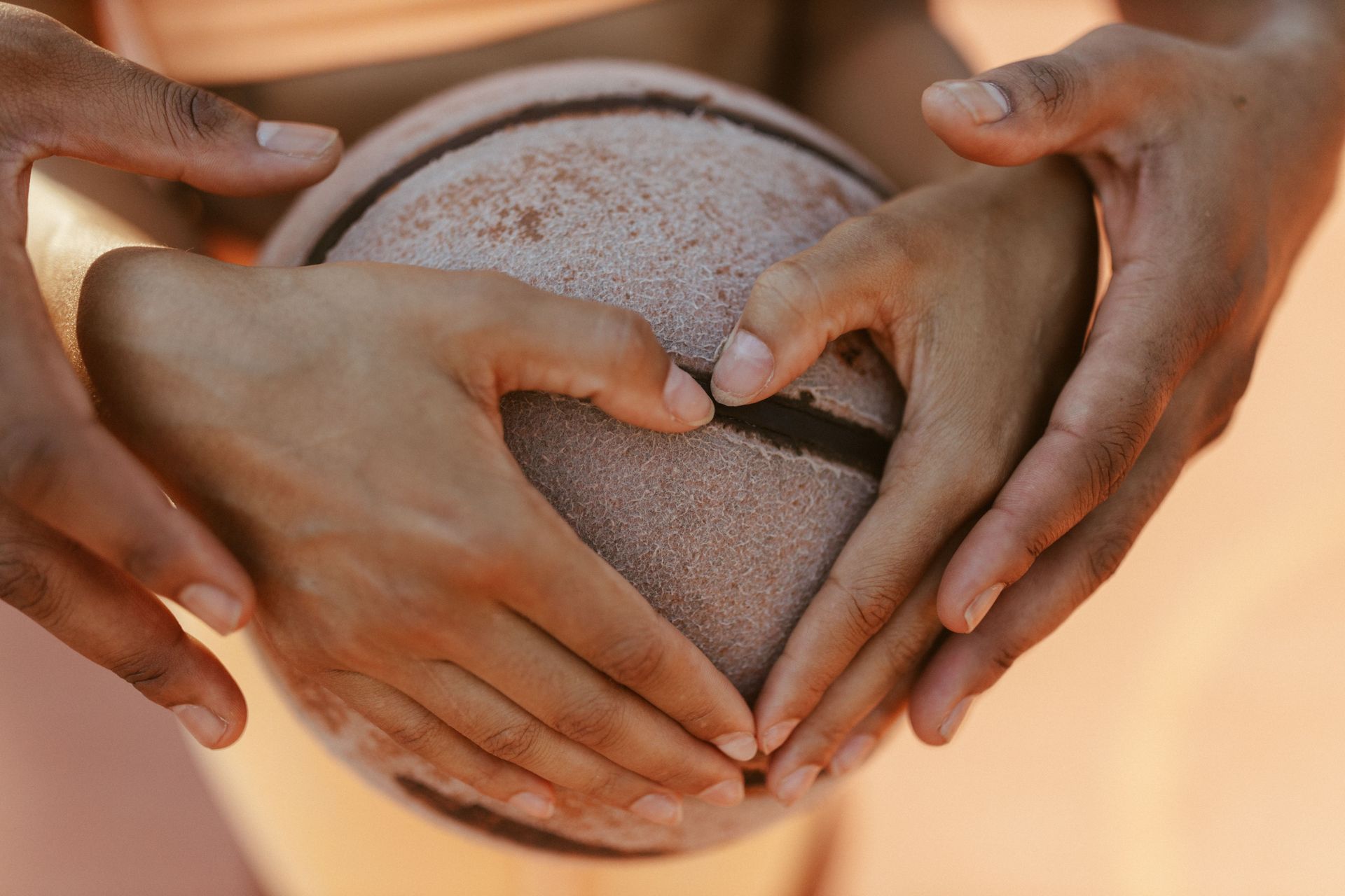 Hands forming a heart around a textured ball on a warm, blurred background