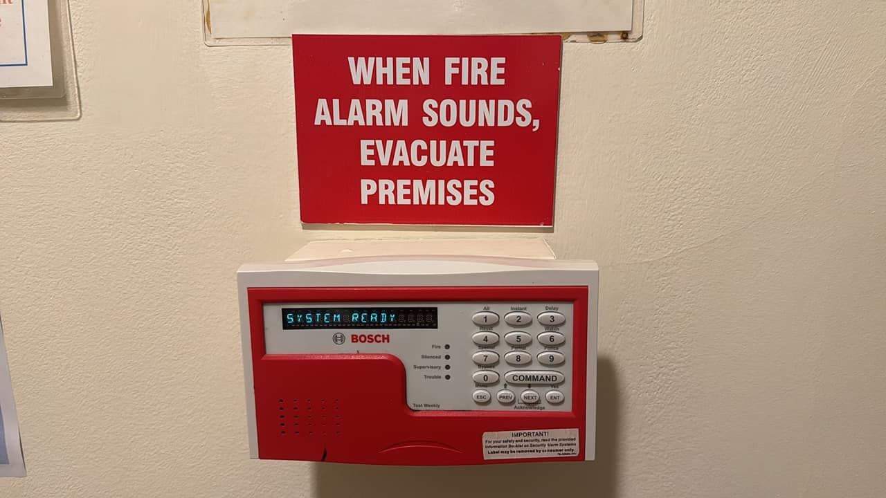 Red fire alarm control panel with instructions to evacuate premises, mounted on a wall.