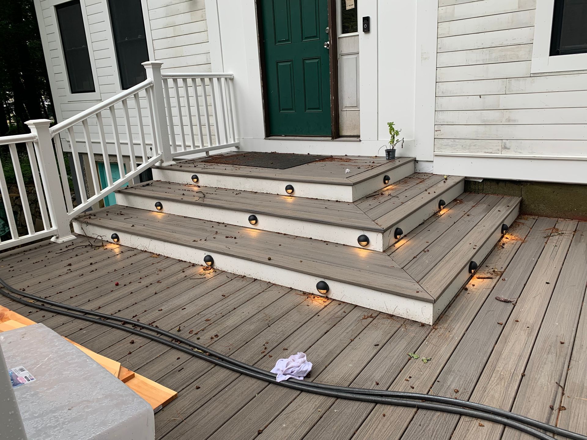 Wooden steps with lights leading to a green door of a white house.