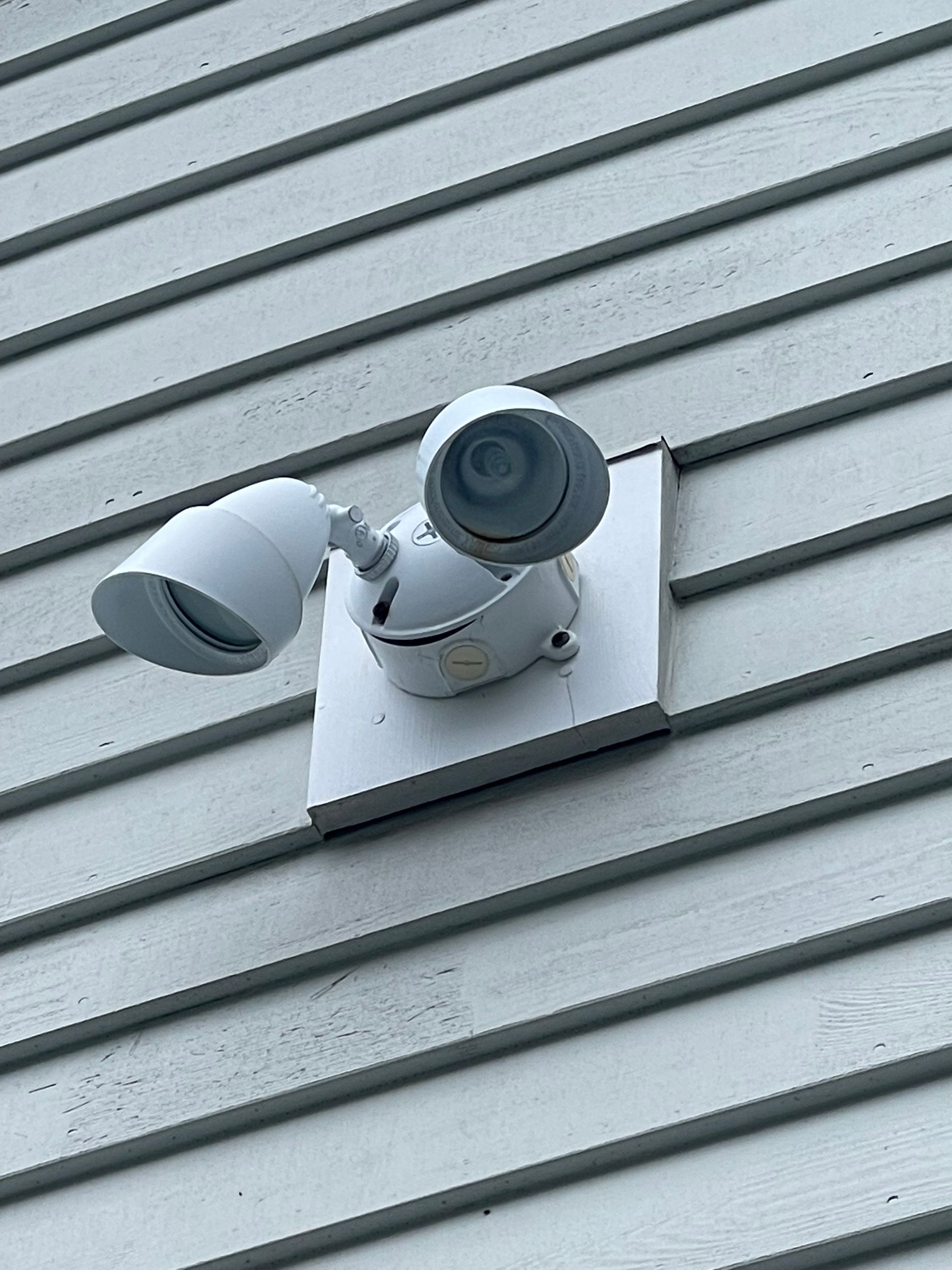 White outdoor security light mounted on white siding.