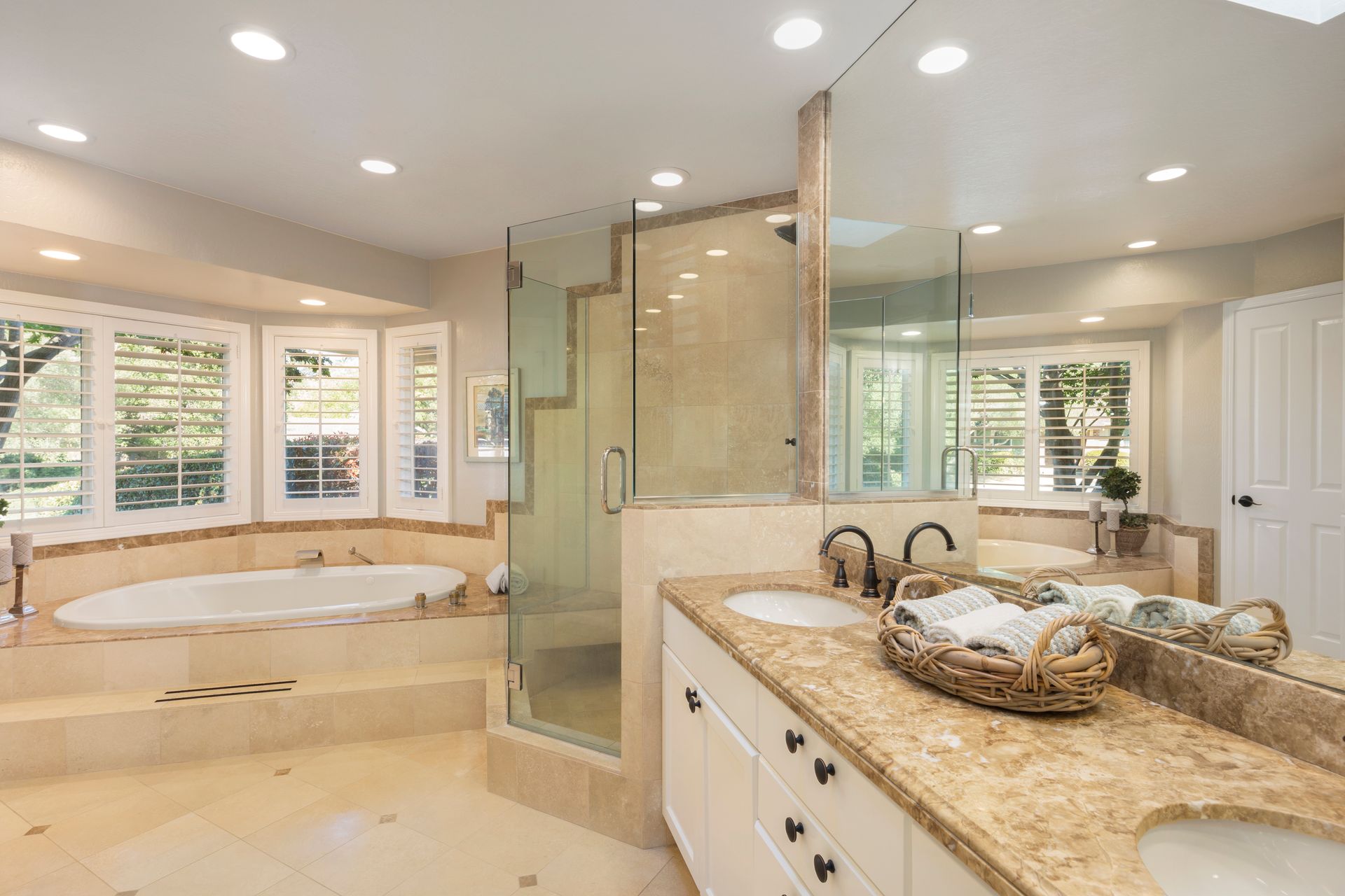 Luxurious beige bathroom with a glass shower, soaking tub, and granite vanity under recessed lights Luxurious beige bathroom with a glass shower, soaking tub, and granite vanity under recessed lights