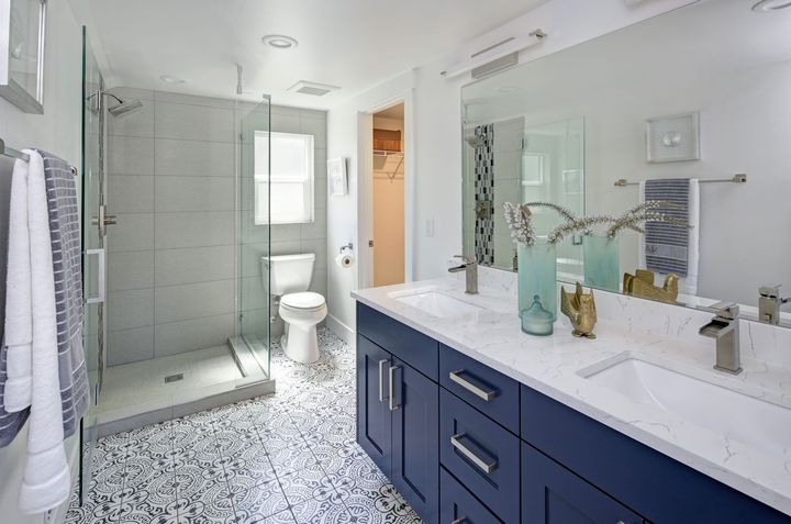 Bright modern bathroom with glass shower, toilet, navy vanity, and white tile floor Bright modern bathroom with glass shower, toilet, navy vanity, and white tile floor