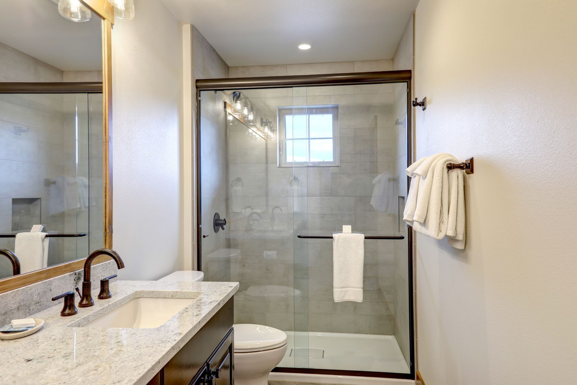 Bright bathroom with granite vanity, large mirror, and glass-enclosed shower with towel rack. Bright bathroom with granite vanity, large mirror, and glass-enclosed shower with towel rack.