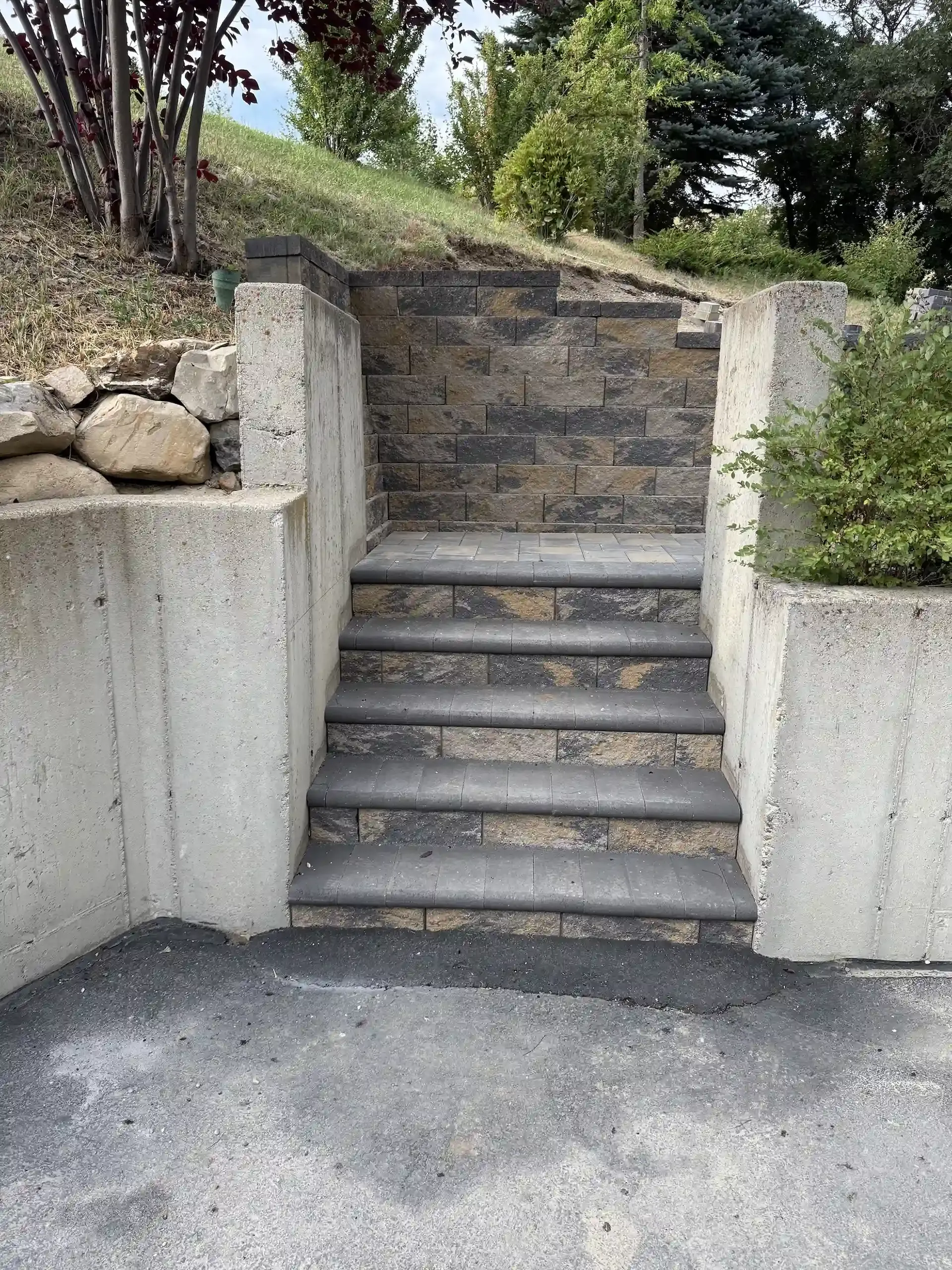 Stone steps with concrete sides and retaining wall on a hillside, asphalt below.