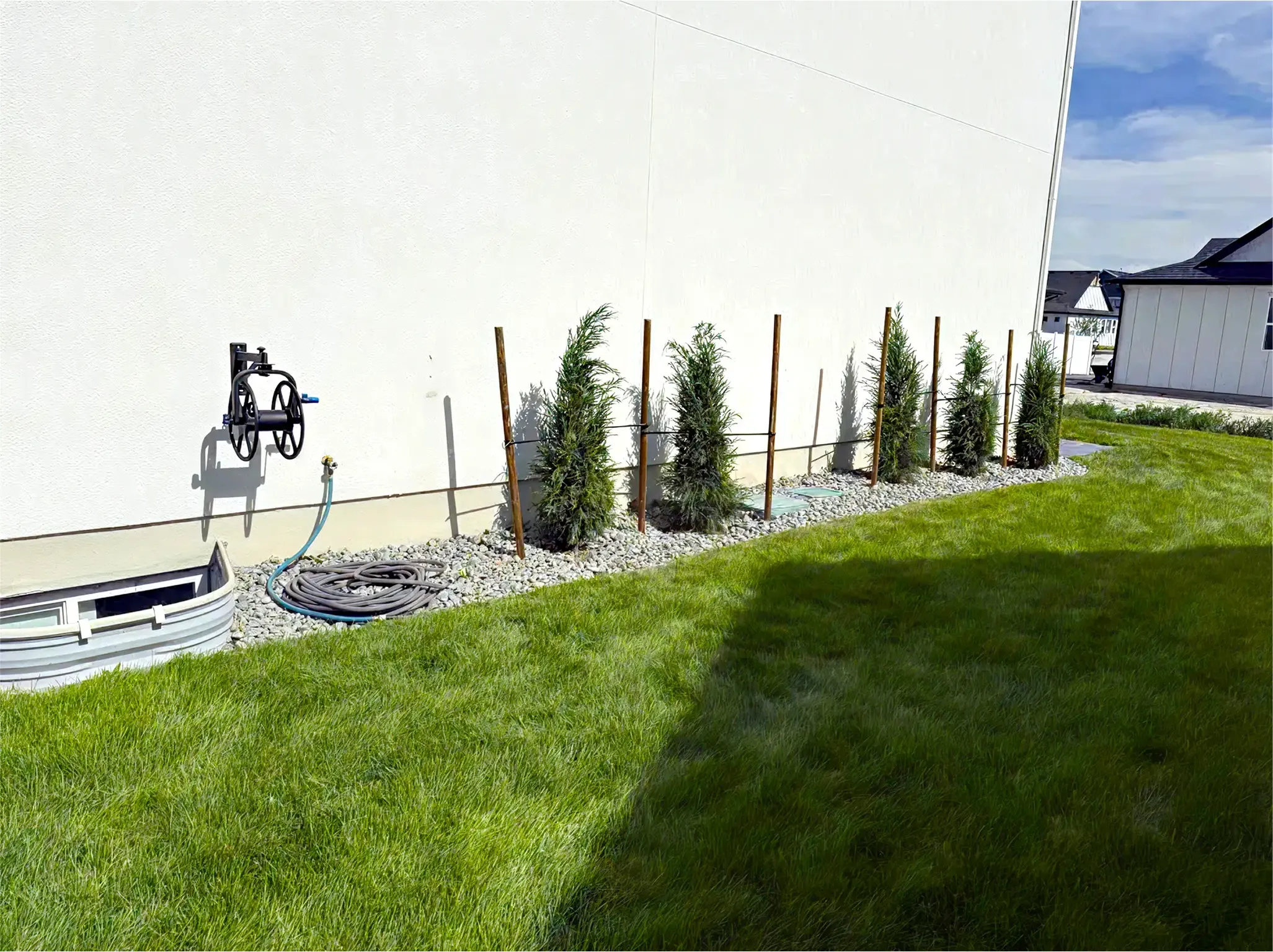 A white house with a green lawn. Small trees are planted next to the house, held up by wooden stakes.