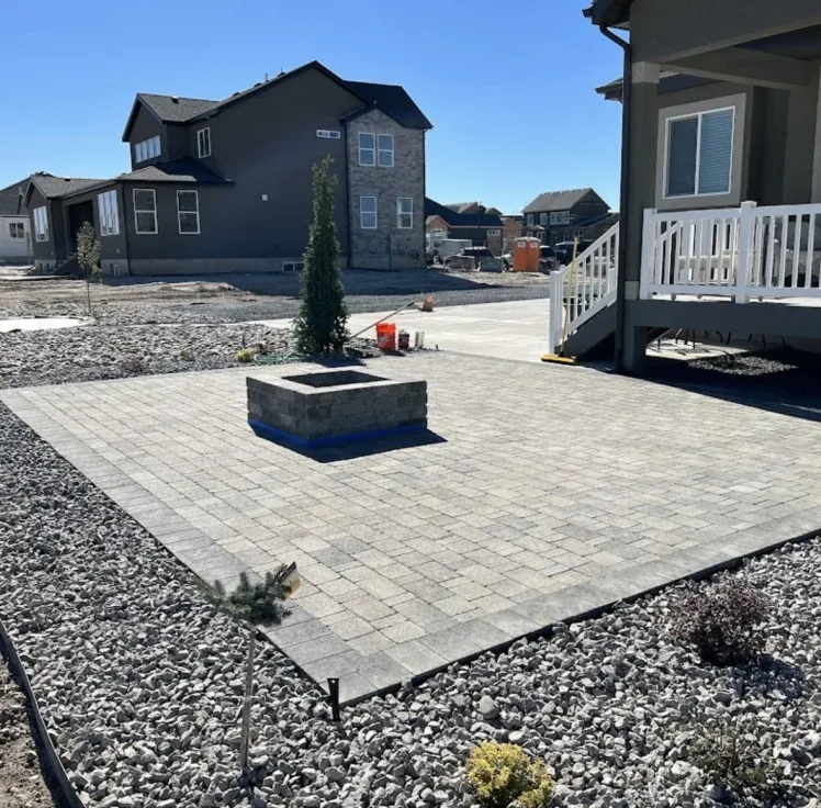 Paver patio with fire pit, bordered by gravel, in a suburban backyard.