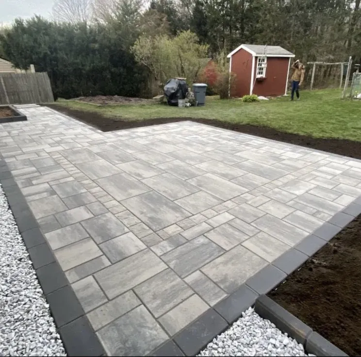 Finished patio with gray pavers and border, next to a grassy lawn with a small shed.