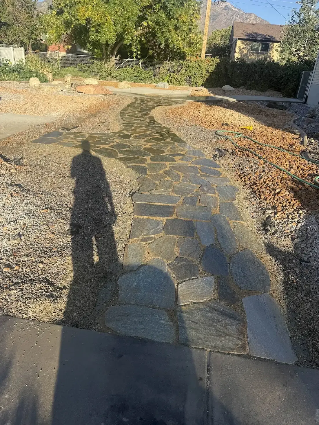Stone pathway through a gravel yard. A shadow of a person falls on the stones.