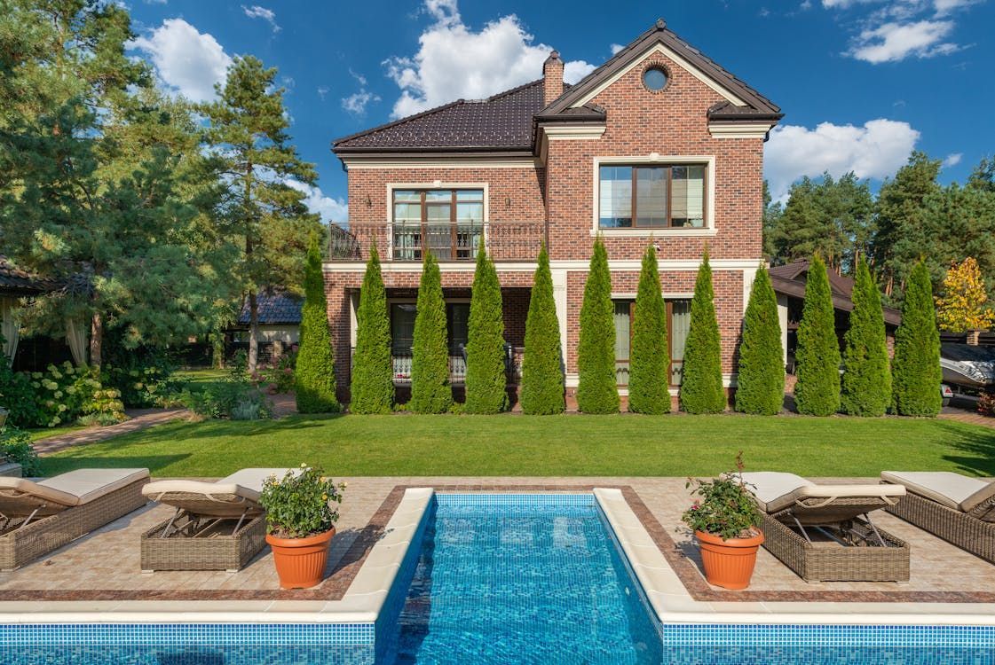 Brick house with pool, lawn, and evergreen trees. Sunny day. Brick house with pool, lawn, and evergreen trees. Sunny day.