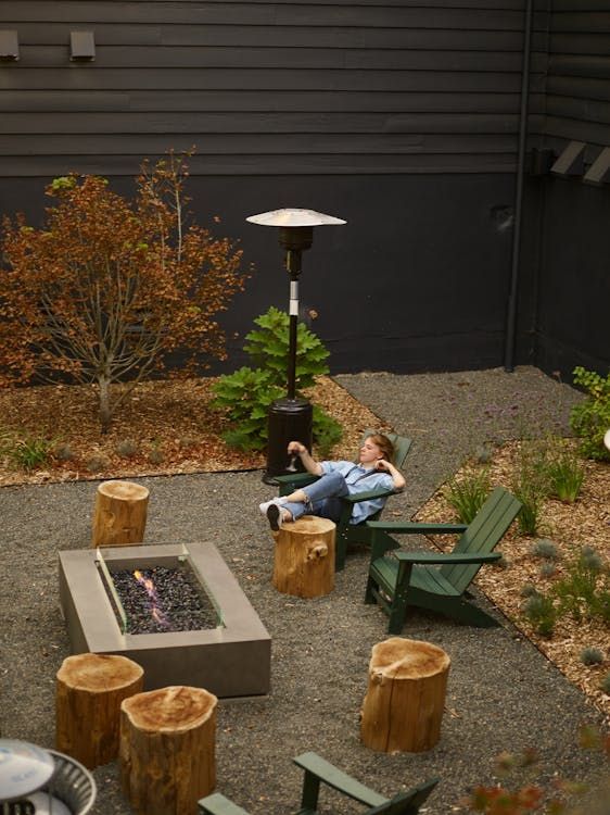 Person relaxing in a backyard with a fire pit, stumps, and a patio heater. Person relaxing in a backyard with a fire pit, stumps, and a patio heater.