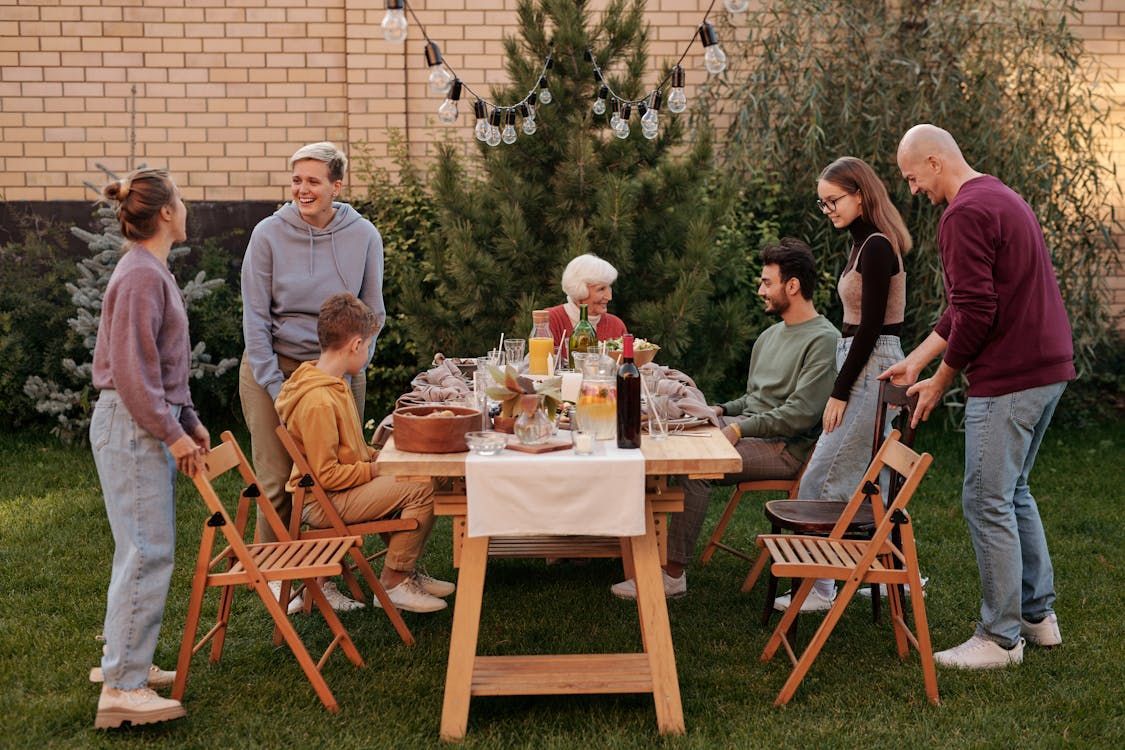 Family gathered around a wooden table in a backyard, preparing for a meal. Family gathered around a wooden table in a backyard, preparing for a meal.