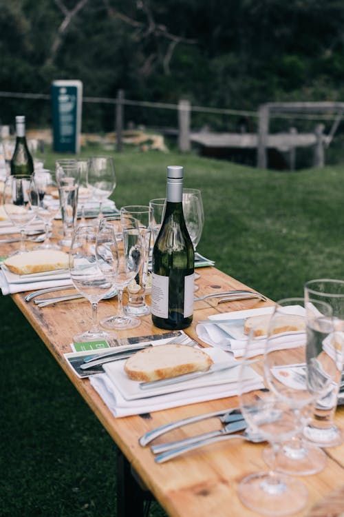 Outdoor table set for a meal with wine bottles, glasses, plates. Outdoor table set for a meal with wine bottles, glasses, plates.