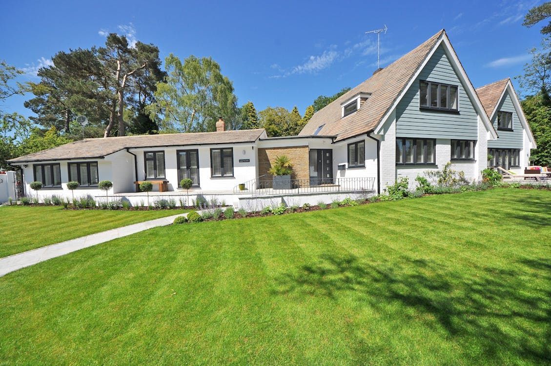 White house with light blue gables, black-framed windows, and a green lawn under a blue sky.