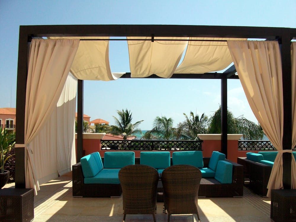 Outdoor lounge area with turquoise cushions, tan curtains, and a view of the ocean. Outdoor lounge area with turquoise cushions, tan curtains, and a view of the ocean.