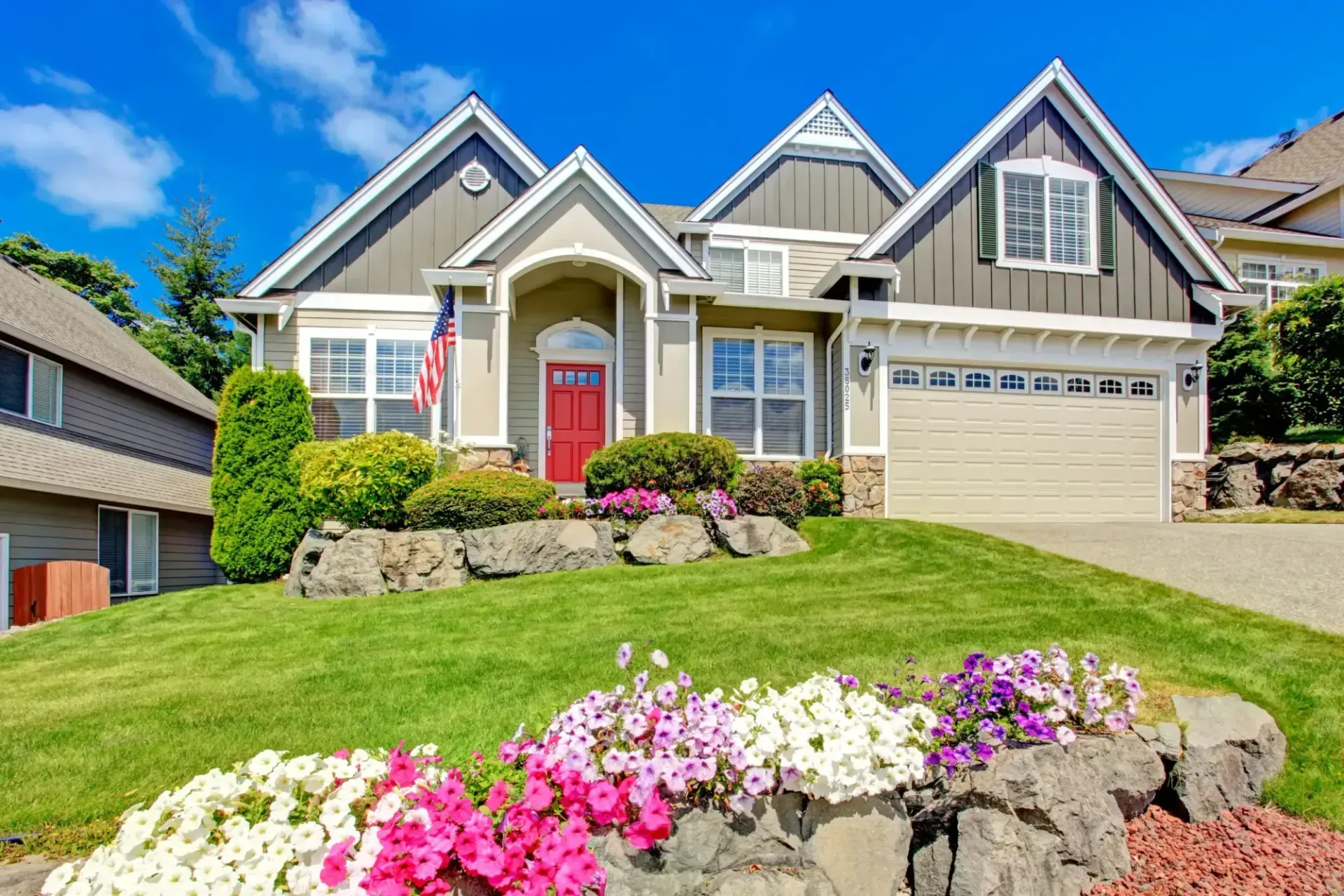 A two-story house with red door, surrounded by lush green lawn and colorful flowers. A two-story house with red door, surrounded by lush green lawn and colorful flowers.
