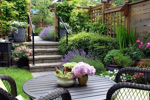 Garden patio with round table and chairs, stone steps, and lush greenery. Garden patio with round table and chairs, stone steps, and lush greenery.