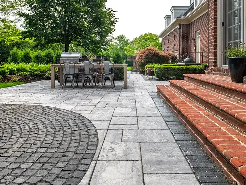 Patio with gray pavers, brick steps, dining table, and green landscaping.