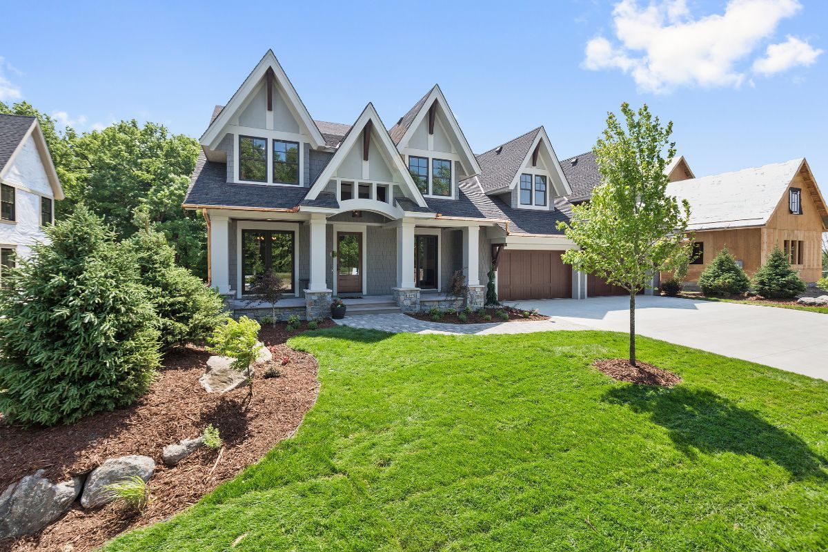 Gray and white house with multiple gables, lush green lawn, and blue sky. Gray and white house with multiple gables, lush green lawn, and blue sky.