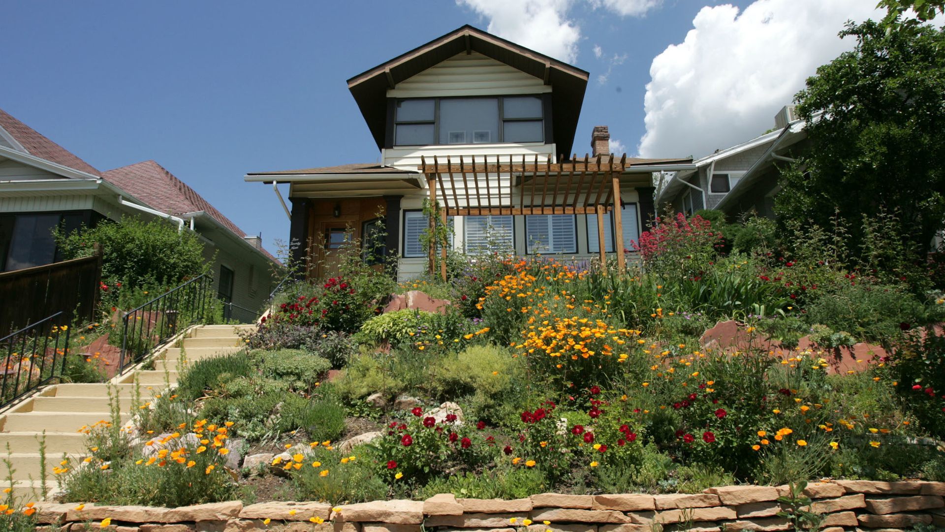 Two-story house with a vibrant, terraced flower garden on a sunny day. Two-story house with a vibrant, terraced flower garden on a sunny day.