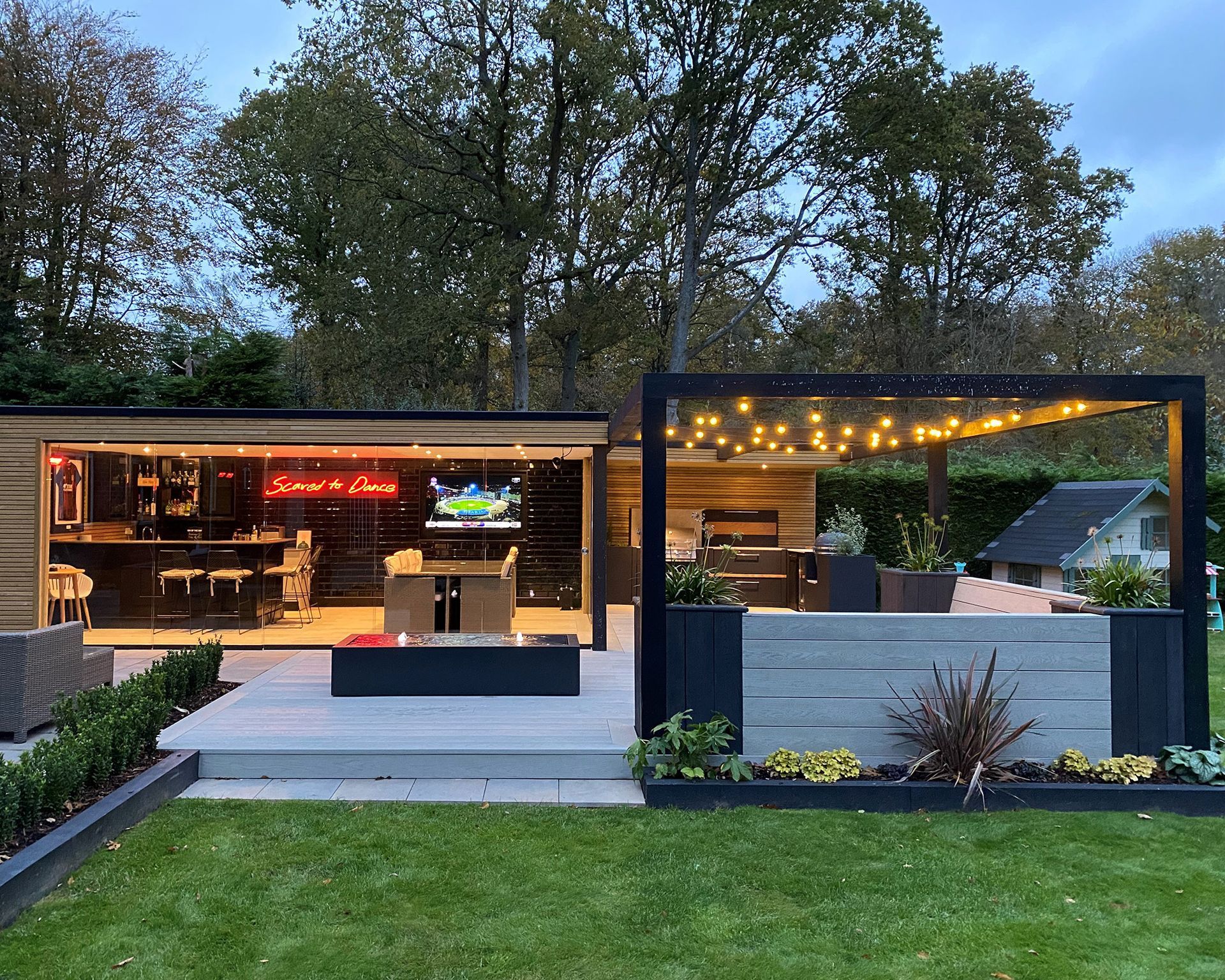 Outdoor entertainment area with bar, seating, and fire pit under string lights. Outdoor entertainment area with bar, seating, and fire pit under string lights.