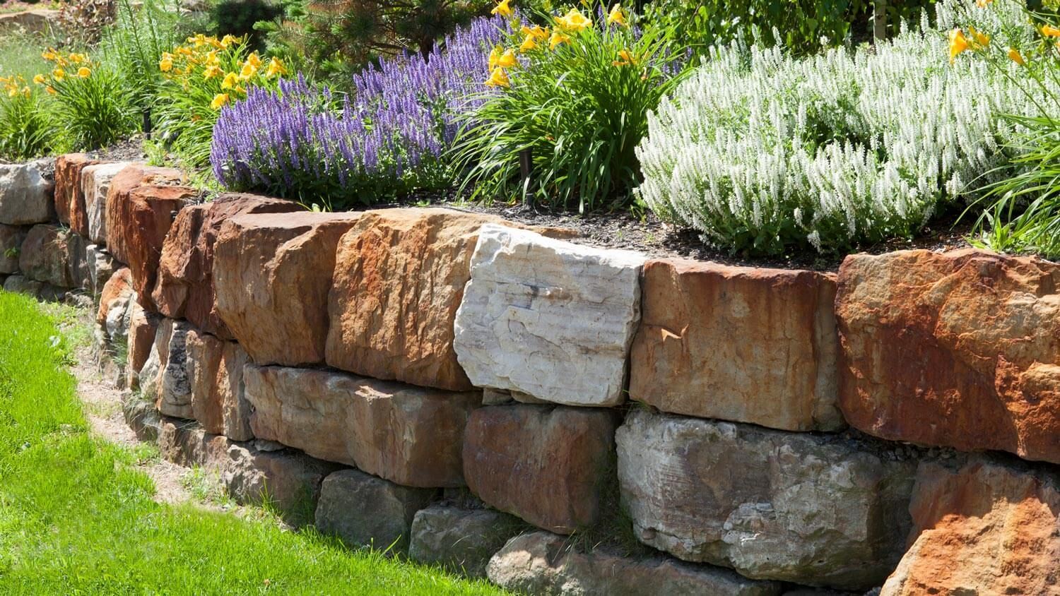 Stone retaining wall with colorful flowers in a garden. Stone retaining wall with colorful flowers in a garden.