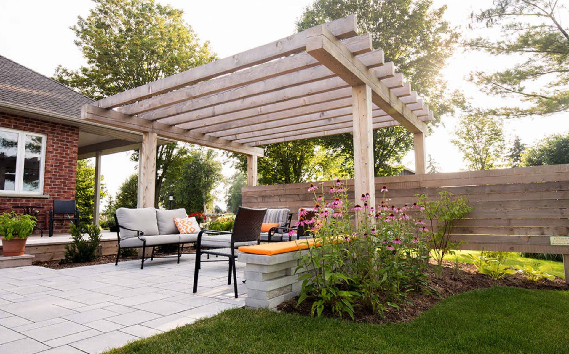 Patio with pergola, outdoor seating, and landscaping next to a red brick house. Patio with pergola, outdoor seating, and landscaping next to a red brick house.