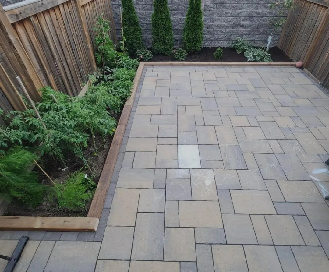 Brick patio with planted garden bed along the side, bordered by a wooden fence.