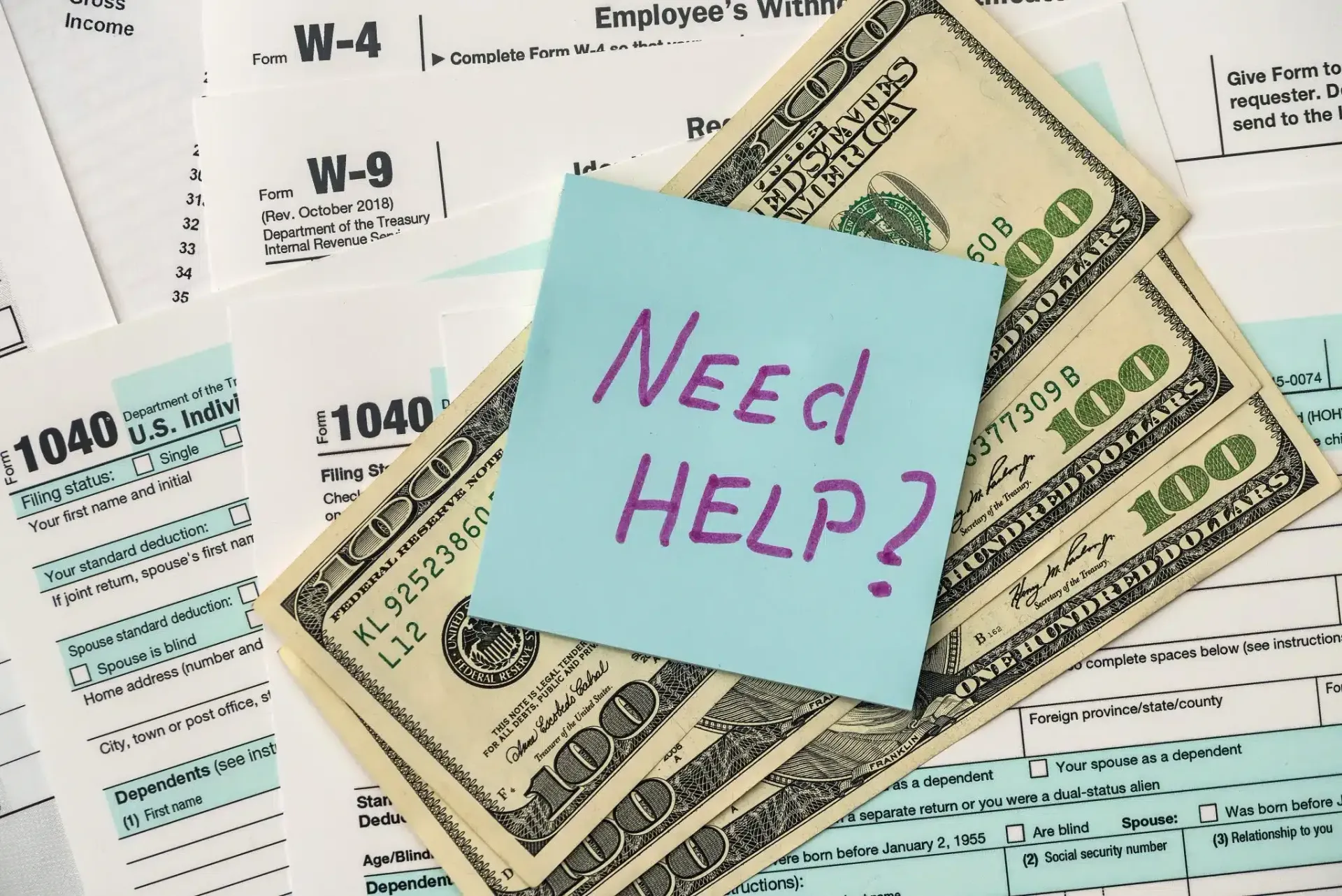 Sticky note reading “Need Help?” over U.S. tax forms and dollar bills