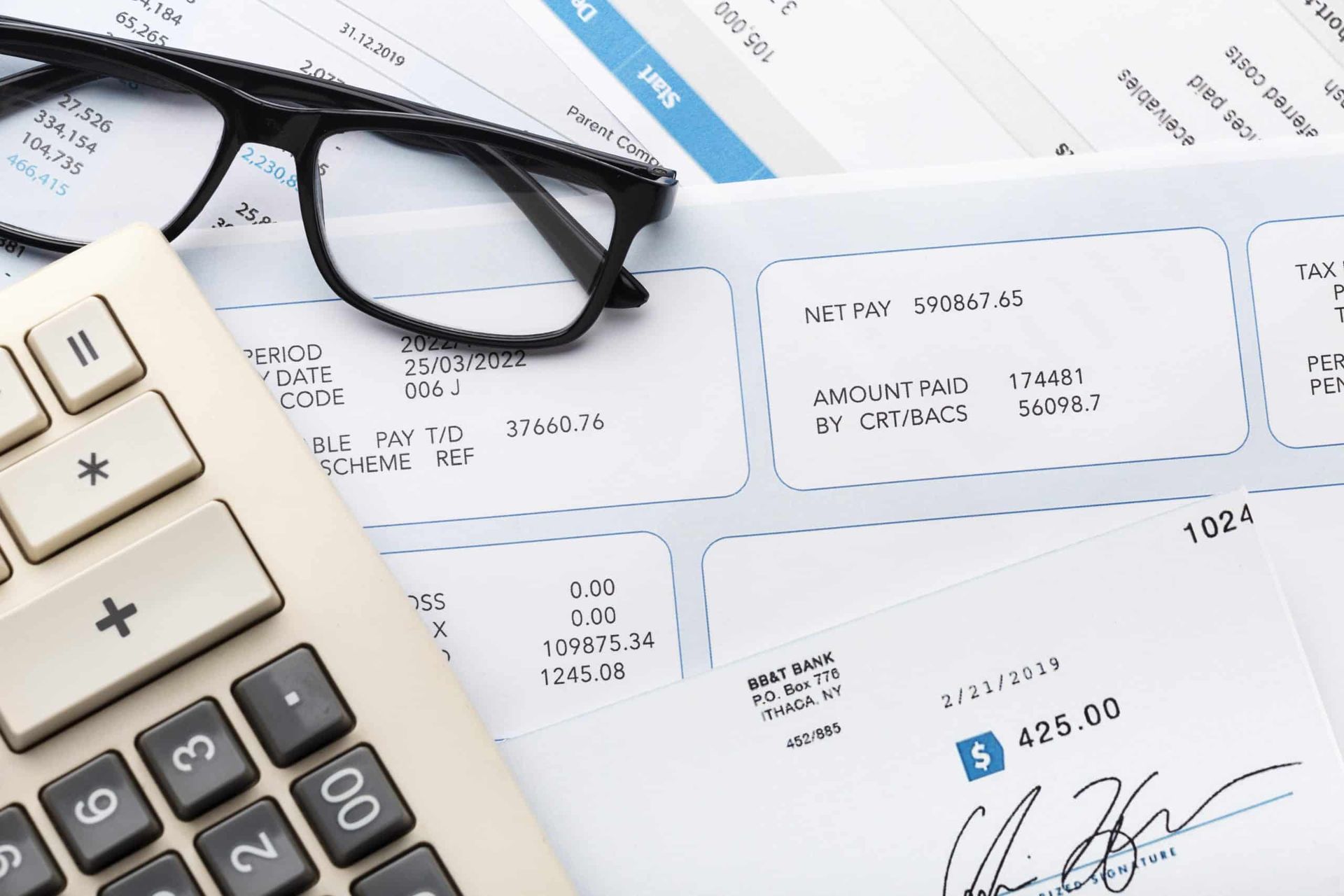 Glasses, calculator, and invoices on a desk, suggesting accounting or bill payment