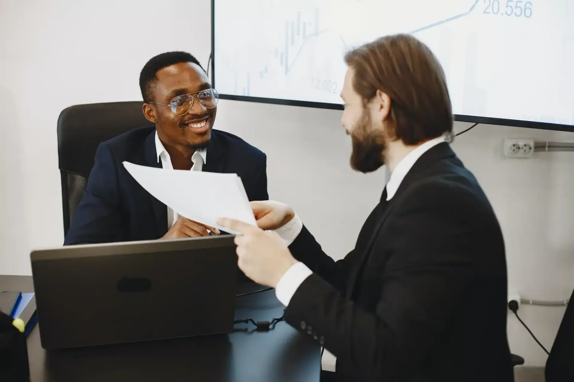 Two people in suits reviewing papers across a conference table in an office meeting room