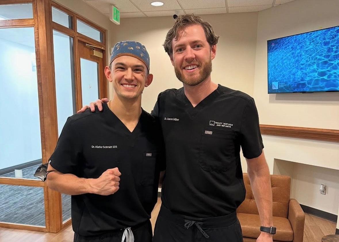 Dr. Aaron Miller smiles with a mentee in black scrubs in a dental office
