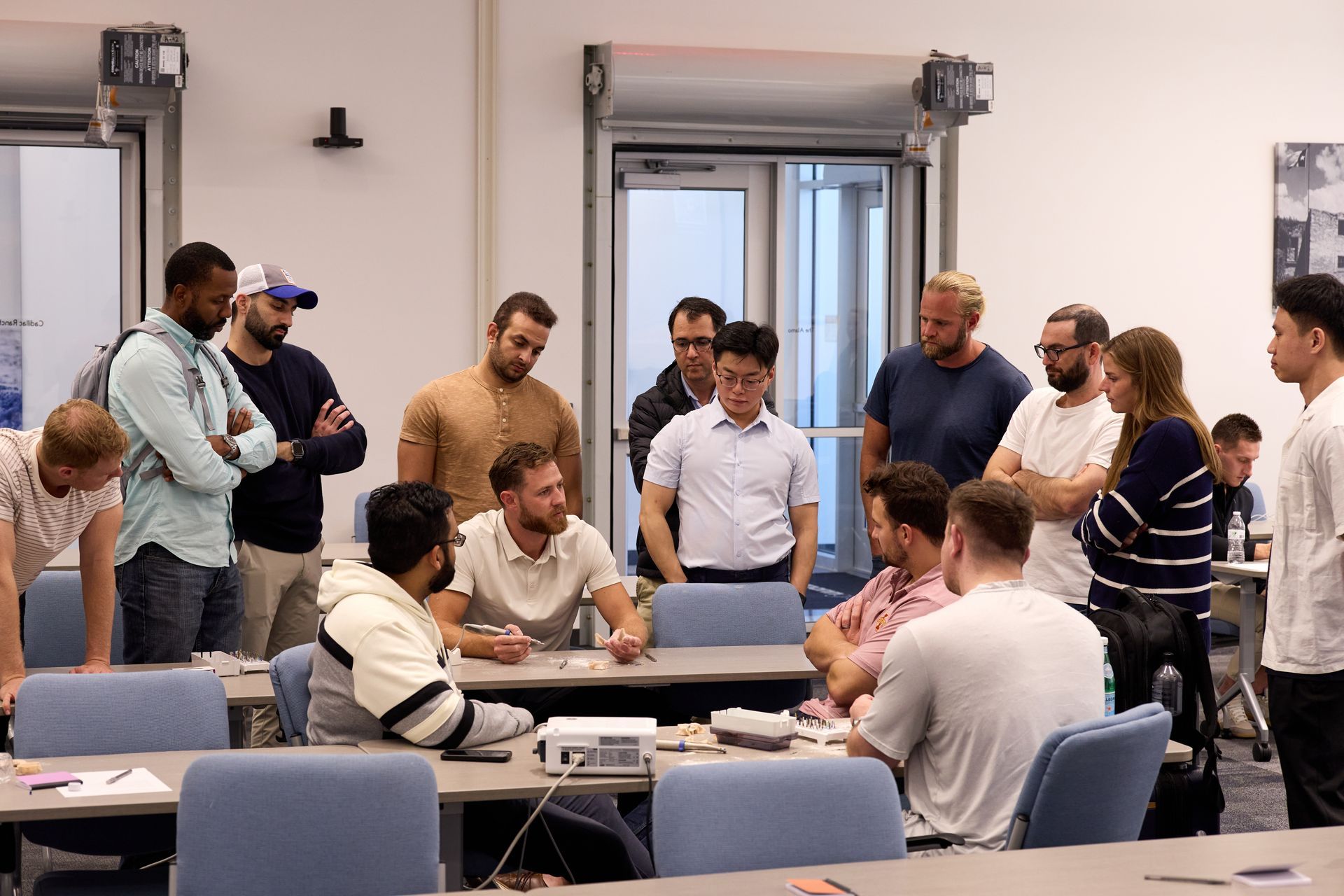 Group of people gathered around Aaron Miller in a meeting room as he teaches full arch procedures.