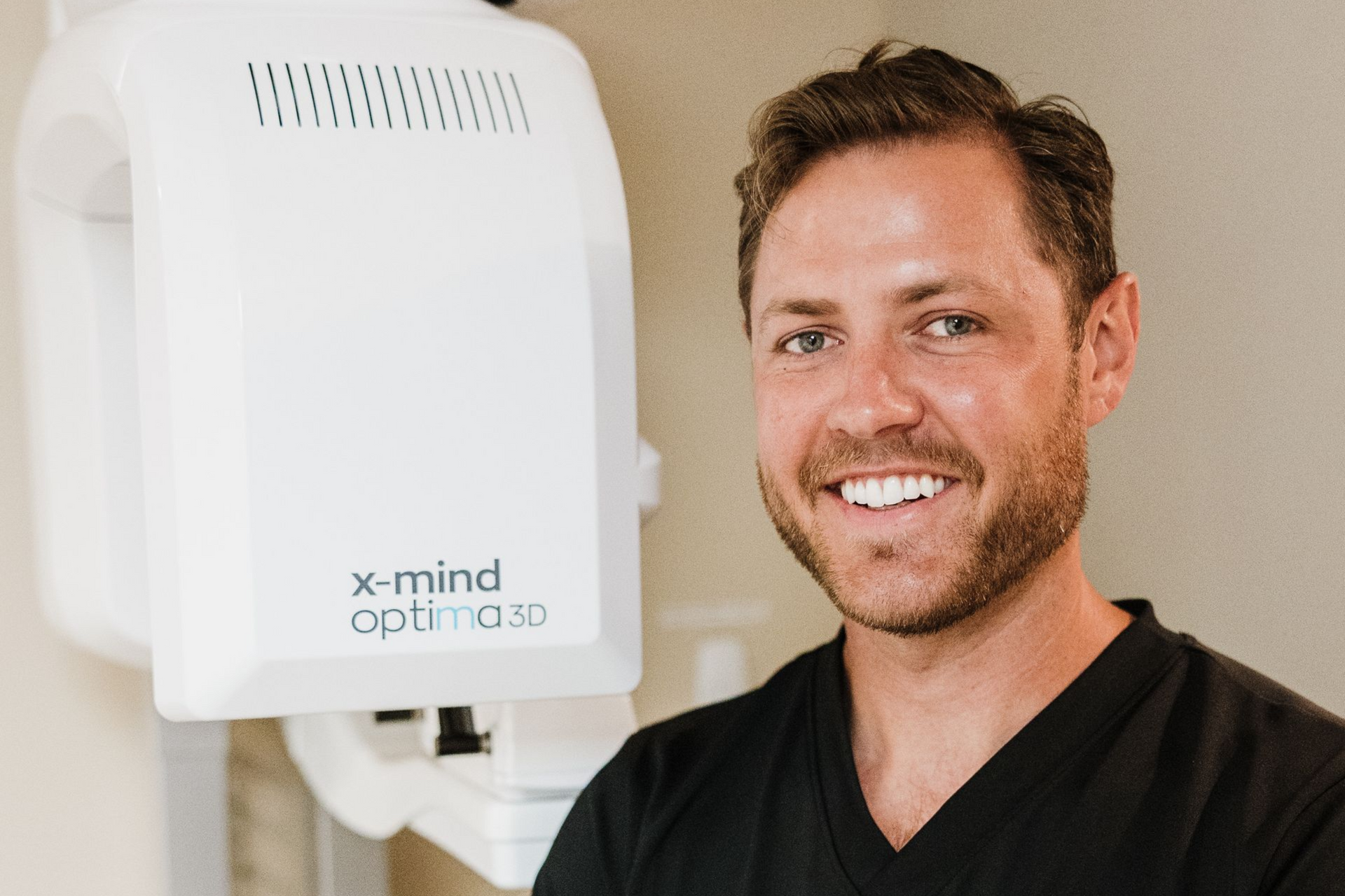 Dr. Aaron Miller smiles beside an X-Mind Optima 3D imaging machine