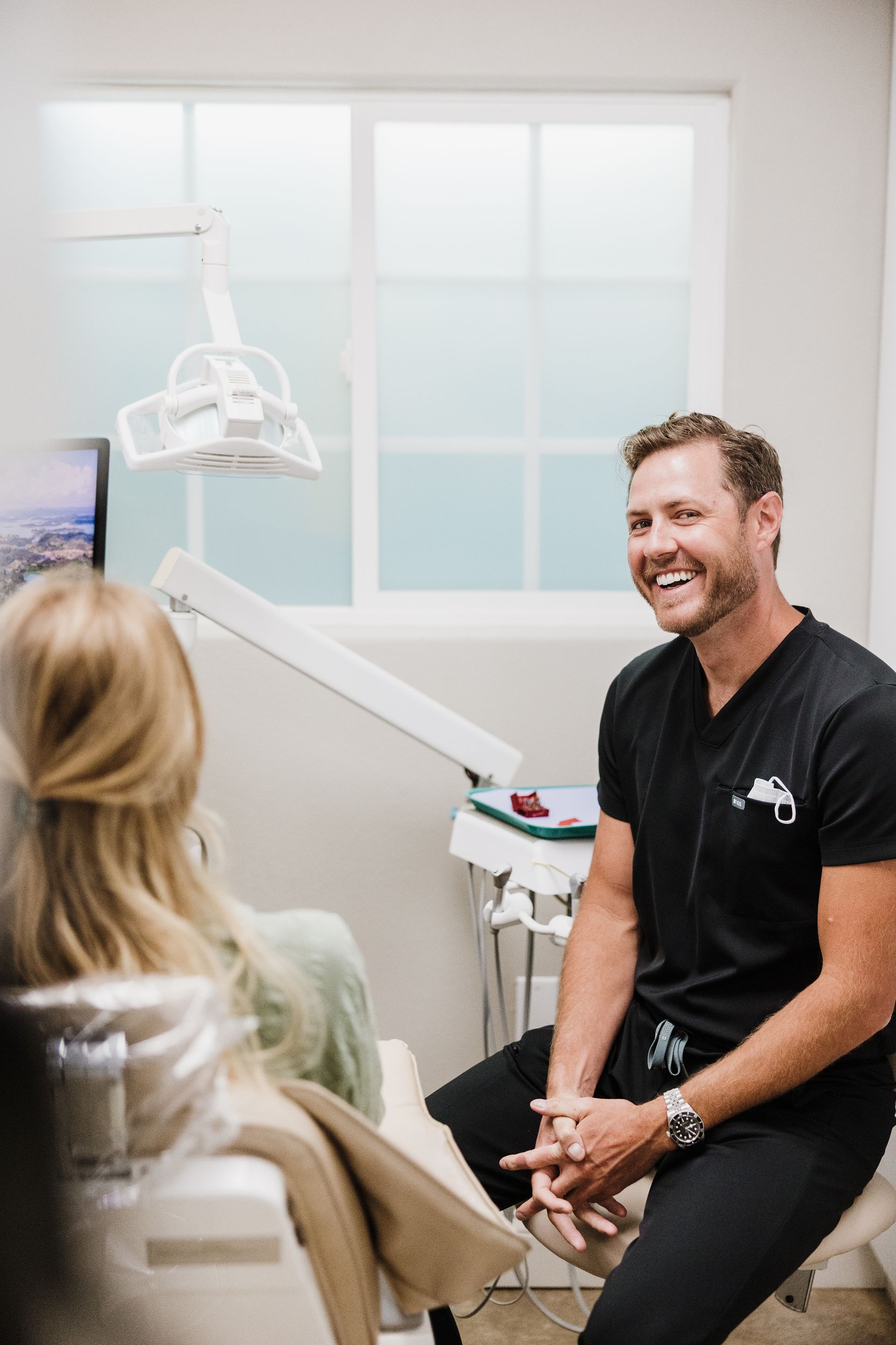 Dr. Aaron Miller smiling at seated patient in a bright dental exam room