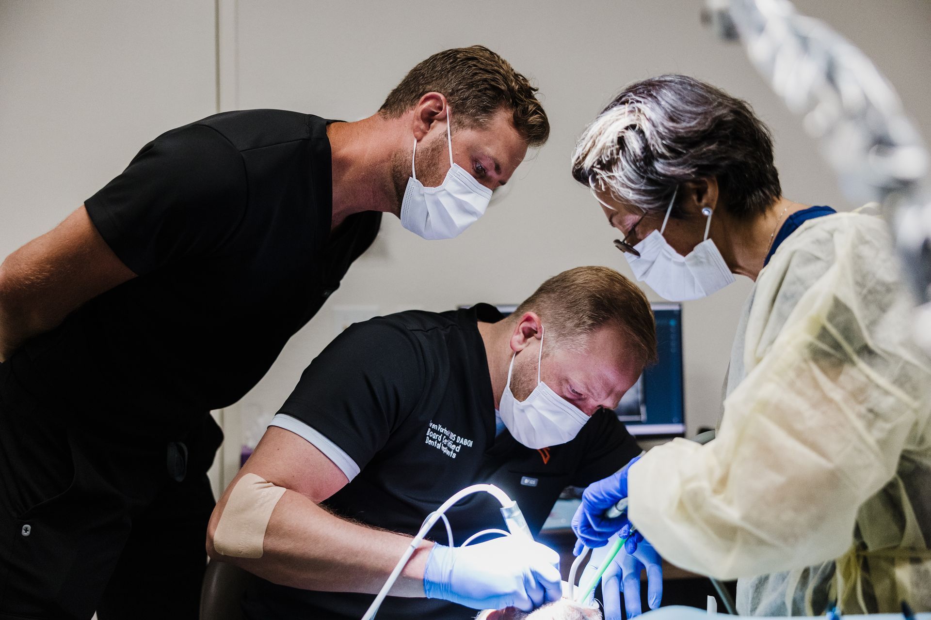 Dr. Aaron Miller looks over another dentist's shoulder as he works on a patient during surgery