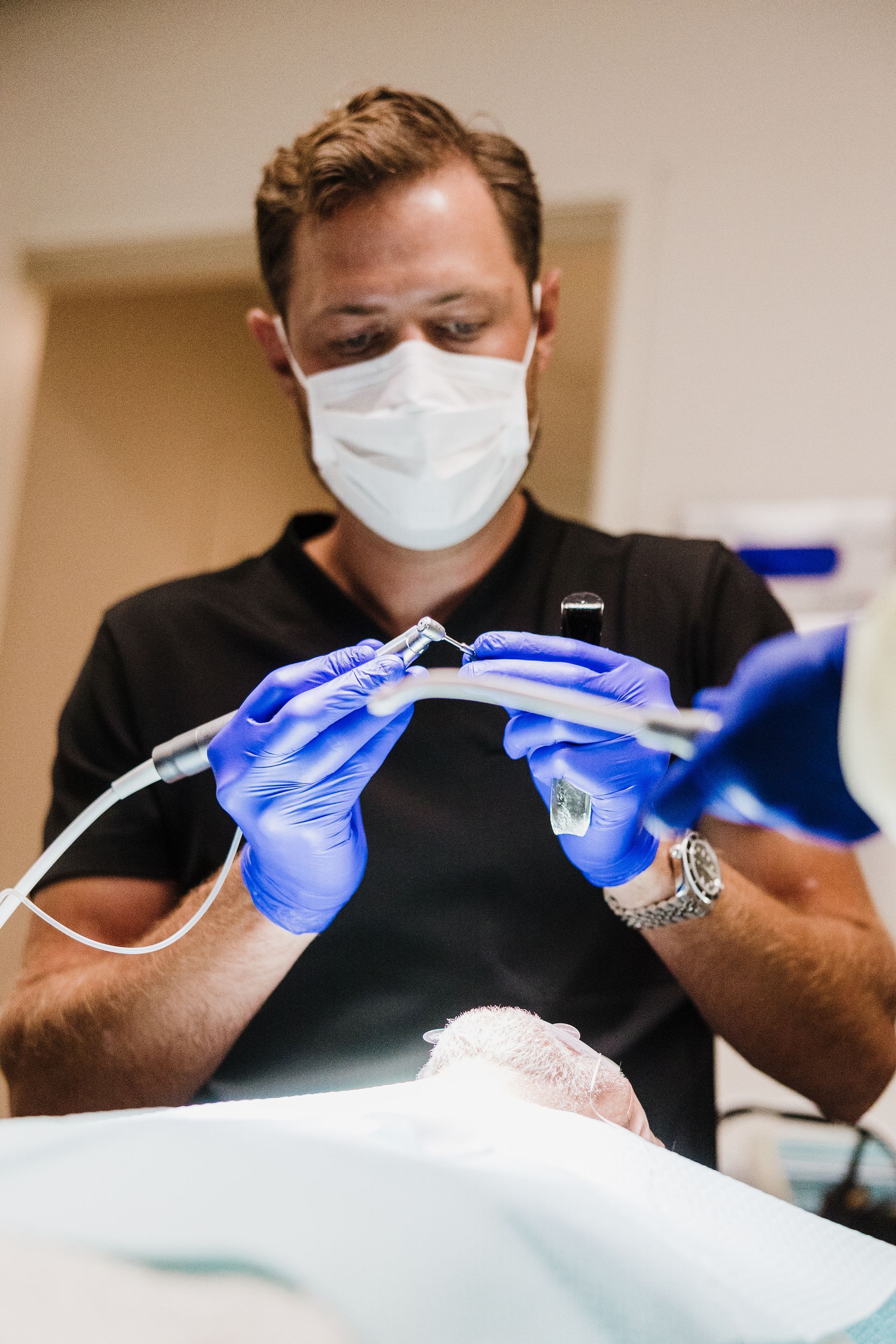 Dr. Aaron Miller wearing a mask and blue gloves examining a patient with dental tools.