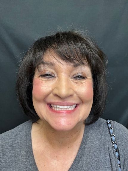 Smiling person with short dark hair against a dark backdrop, wearing a gray top