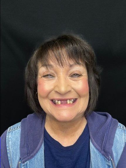 Smiling person with short dark hair, wearing a blue jacket against a black background.