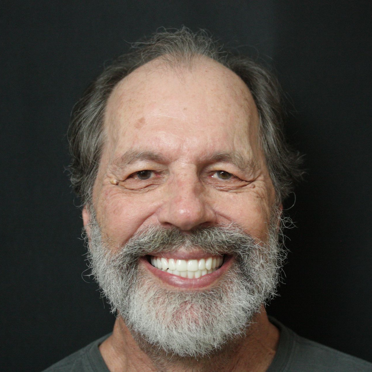 Smiling bearded man with gray hair against a dark background