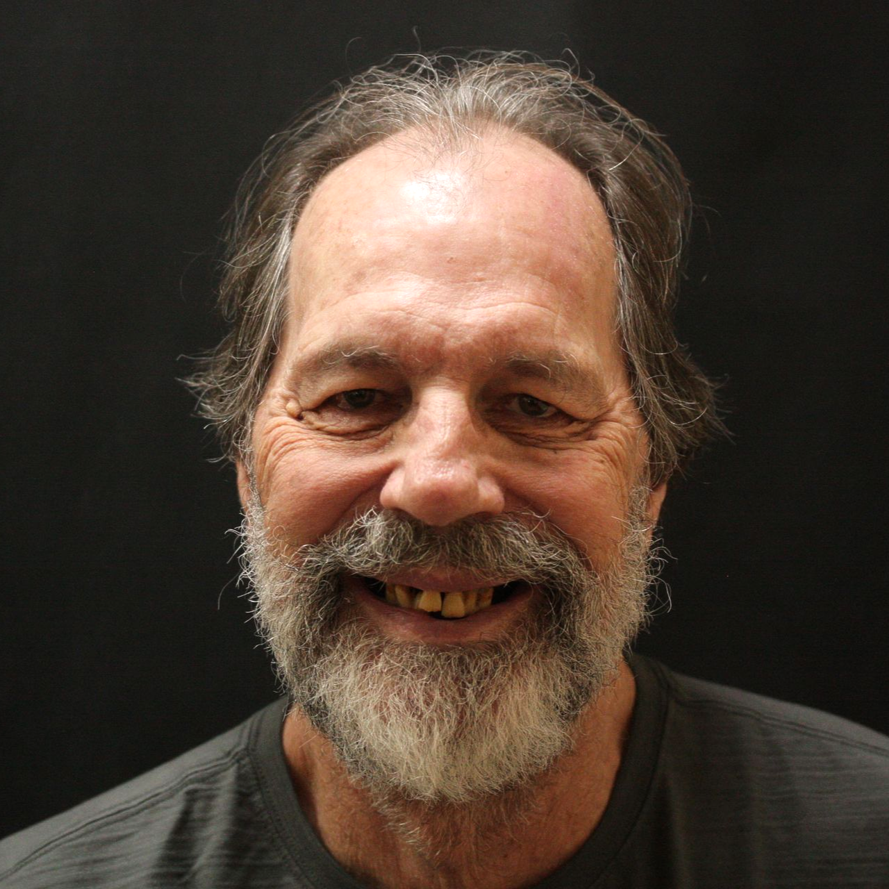 Smiling bearded man with graying hair against a dark background