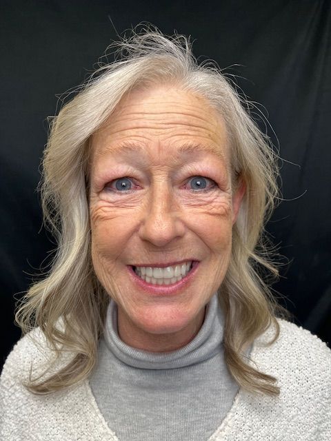 Smiling woman with gray hair against a dark background, wearing a light sweater and turtleneck.