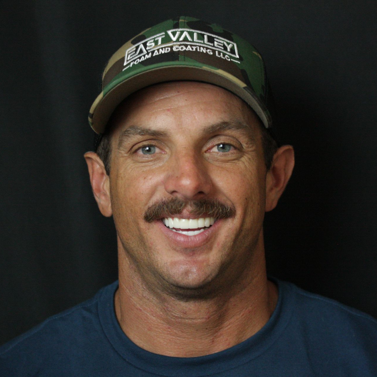 Smiling man in a green cap and navy shirt against a dark background