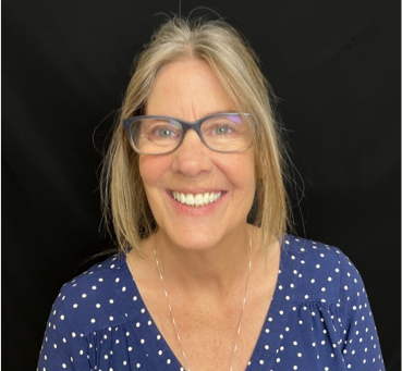 Smiling woman with glasses in a blue polka-dot top against a black background
