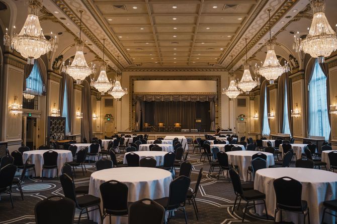 Elegant banquet hall with round tables, chandeliers, and a stage at the far end