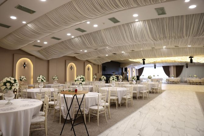 Elegant banquet hall with white-draped tables, gold chairs, and a lit stage at the far end