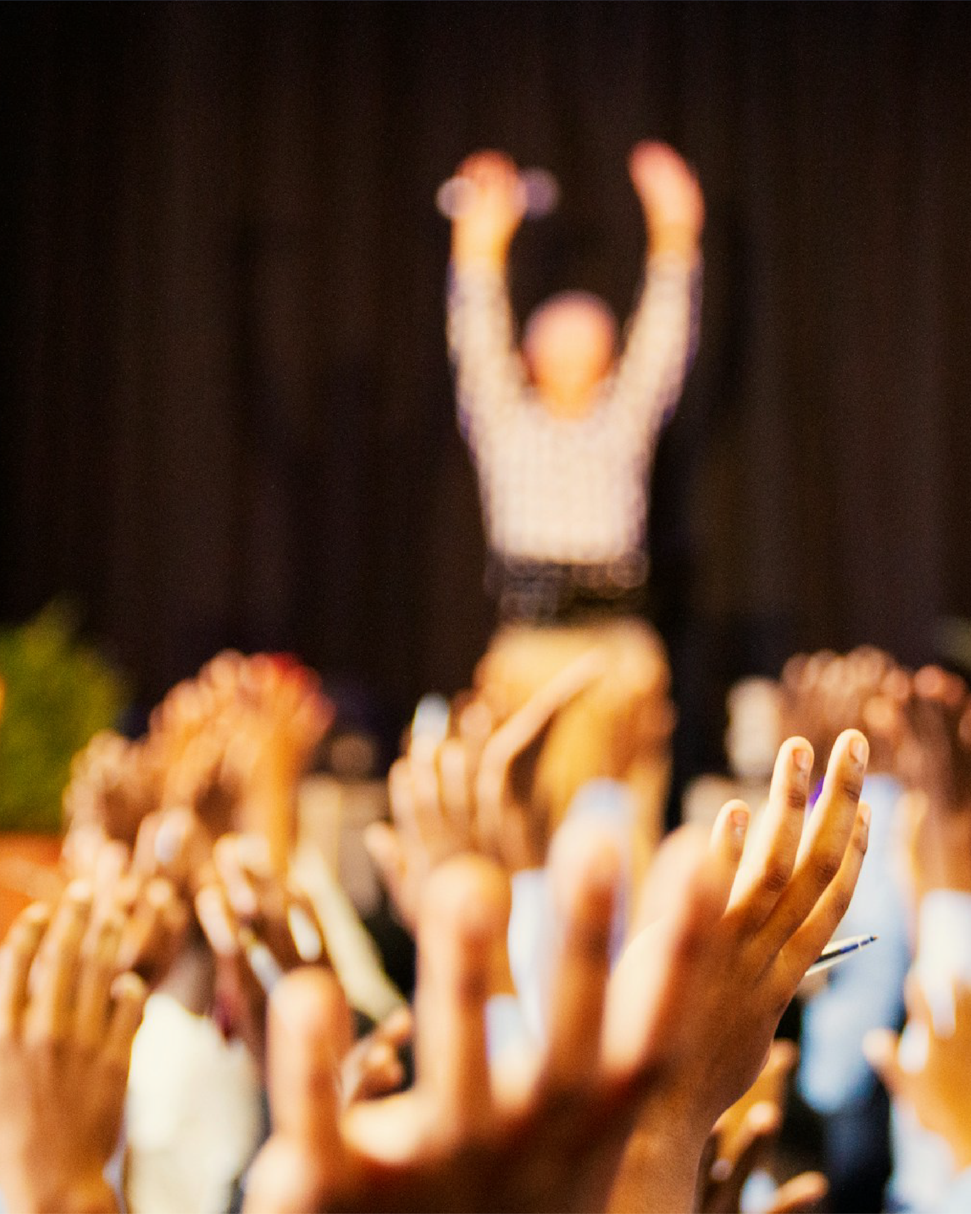 Hands raised toward a blurred figure on stage, holding microphones.