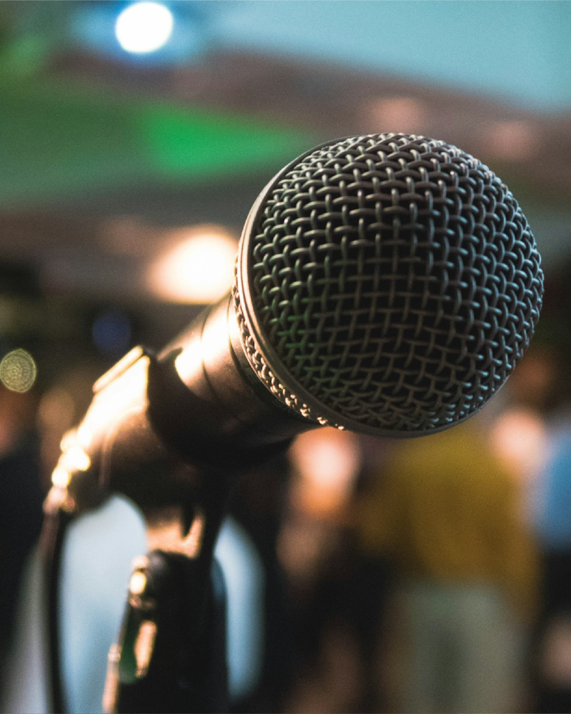 Close-up of a microphone on a stand, blurred background with stage lights and people.