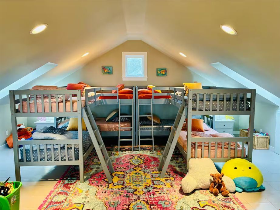 Attic bedroom with two gray bunk beds, colorful rug, and stuffed animals on the floor